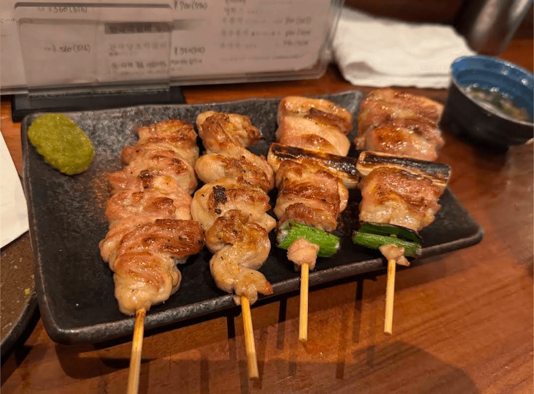 Four skewers of grilled chicken yakitori on a black plate with green yuzukosho paste.
