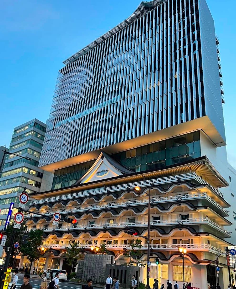 Modern skyscraper built atop a traditional Japanese building with tiered roofs and white walls.