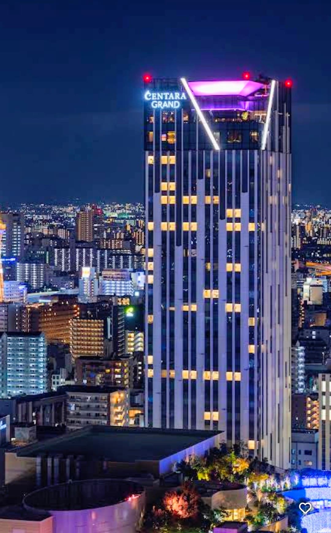 Centara Grand skyscraper with purple rooftop lights overlooking a glowing city skyline at night.