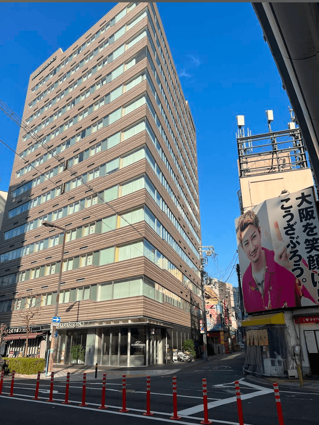 Tall brown building next to a large billboard on a sunny city street corner.