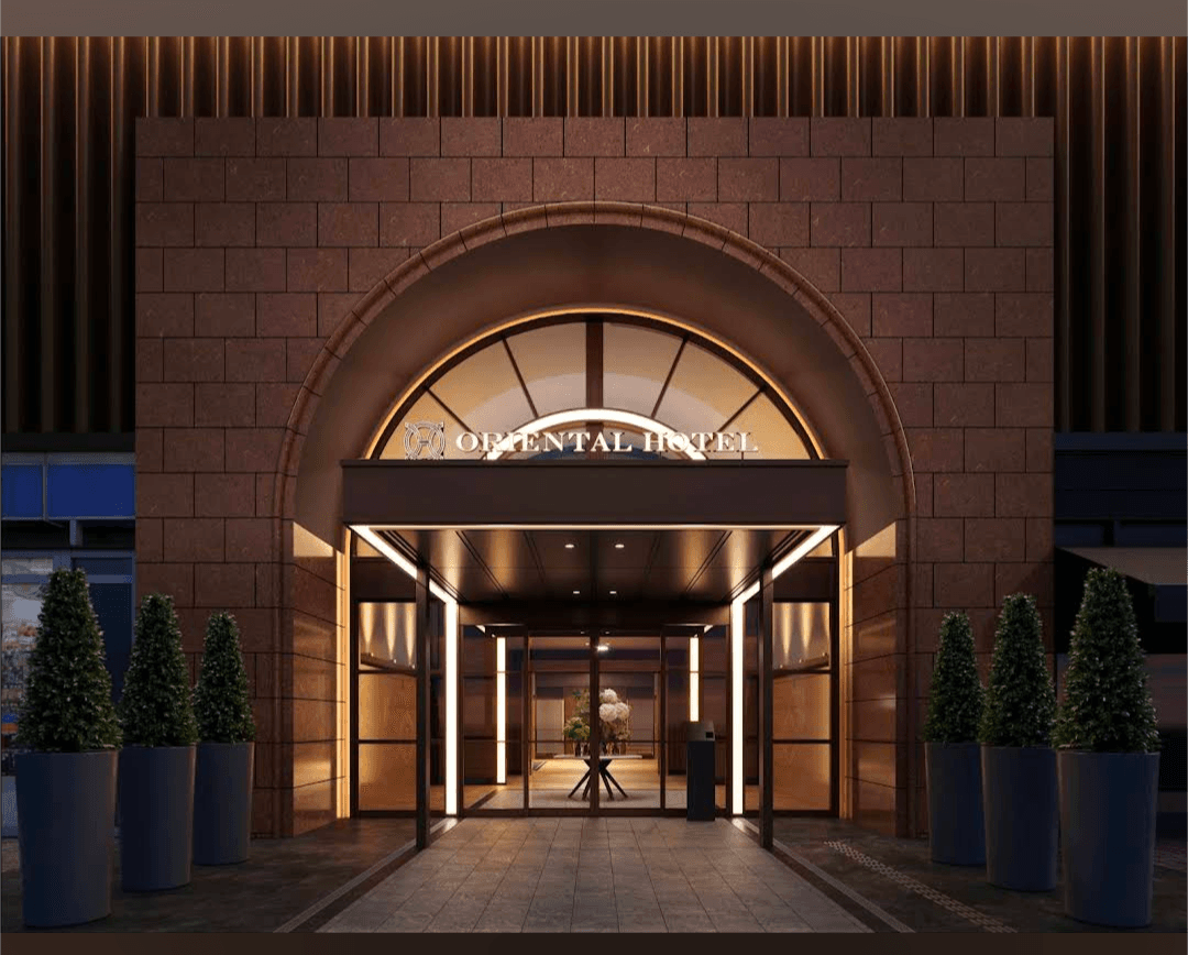Grand arched entrance of the Oriental Hotel with warm lighting and potted evergreen trees.