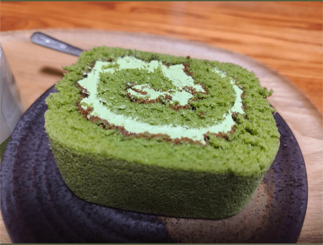 Matcha green tea swiss roll cake slice with light green cream filling on a dark plate.
